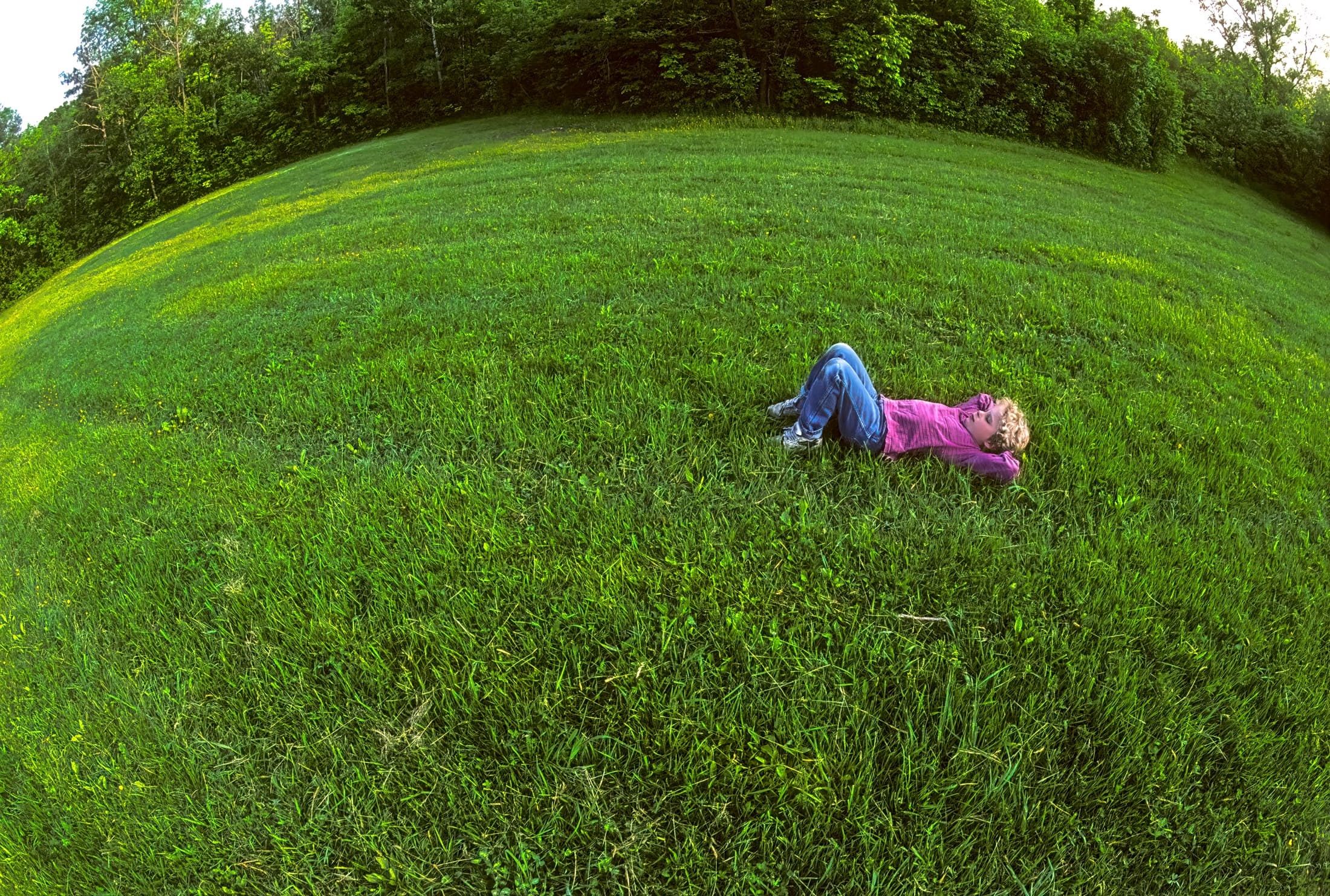 Steinmetz Park, Schenectady, New York. Solitary young boy, thoughtful and daydreaming, lying on a wide expanse of green grass in urban park.