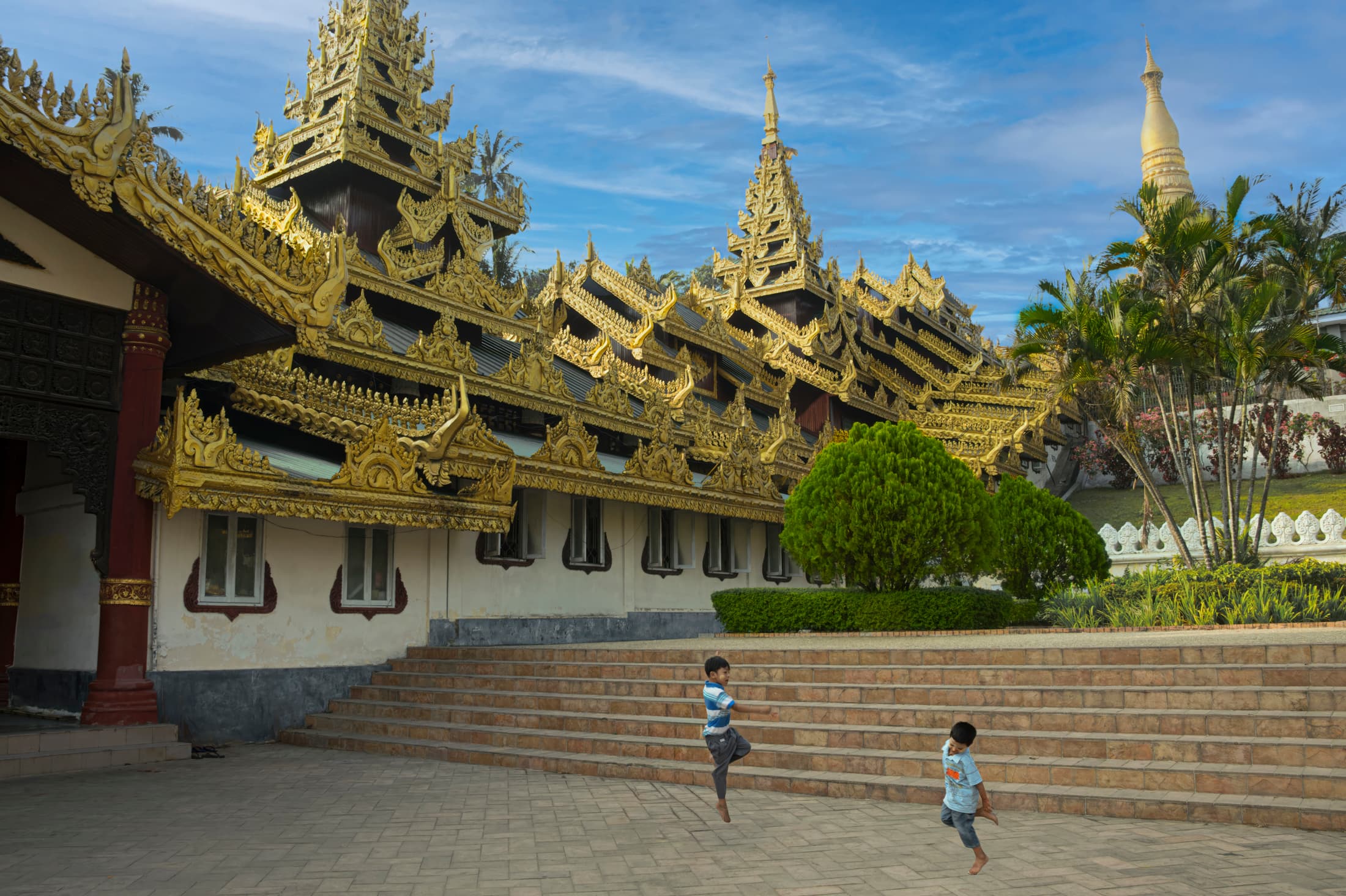 Mya Set Kyar Nunnery. Mandalay, Myanmar. Boy, young monk in red robe walks up white marble steps to temple.