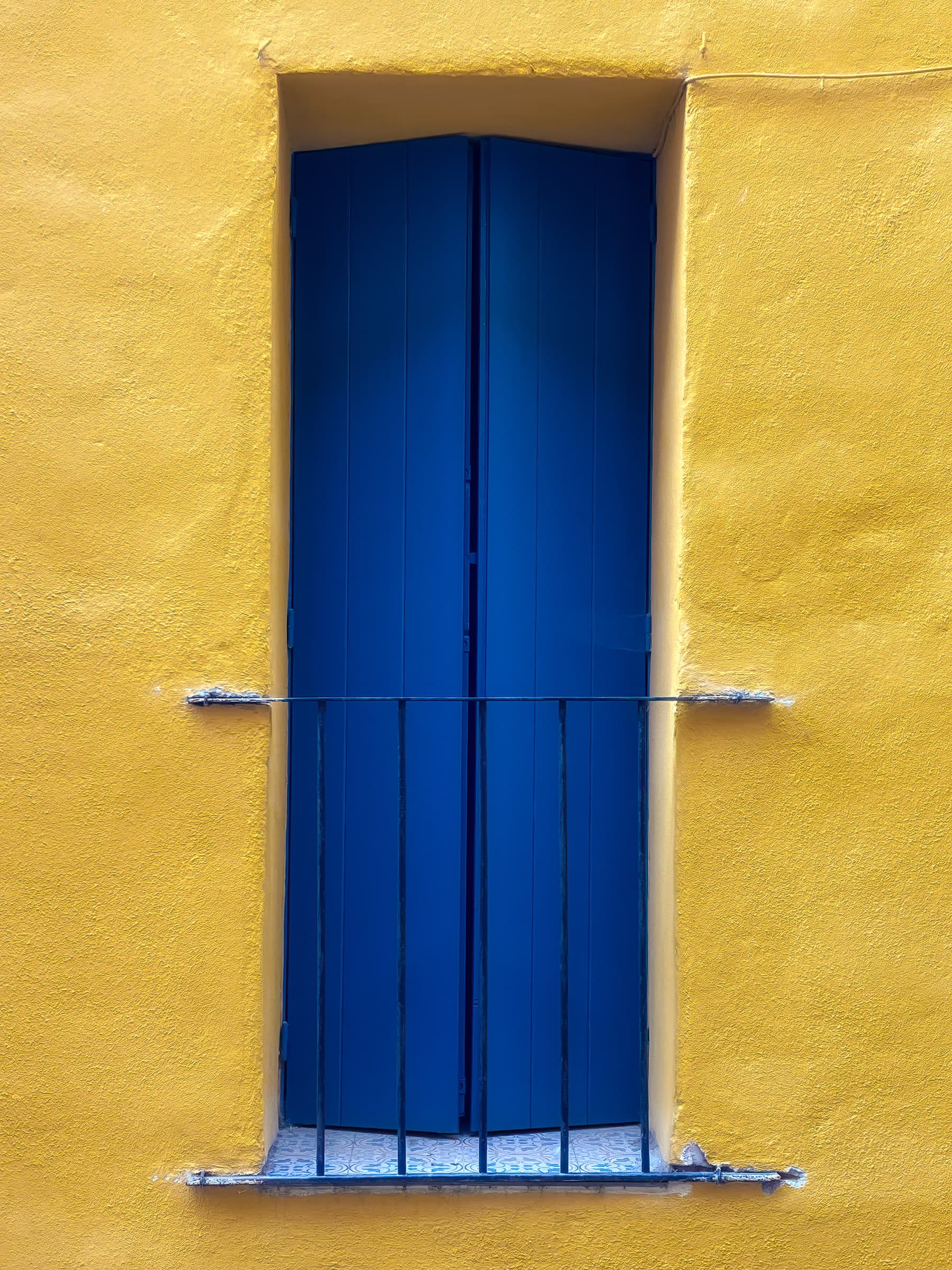 Slightly-open, rectangular, deep-blue window/door set into a bright yellow exterior stucco wall.