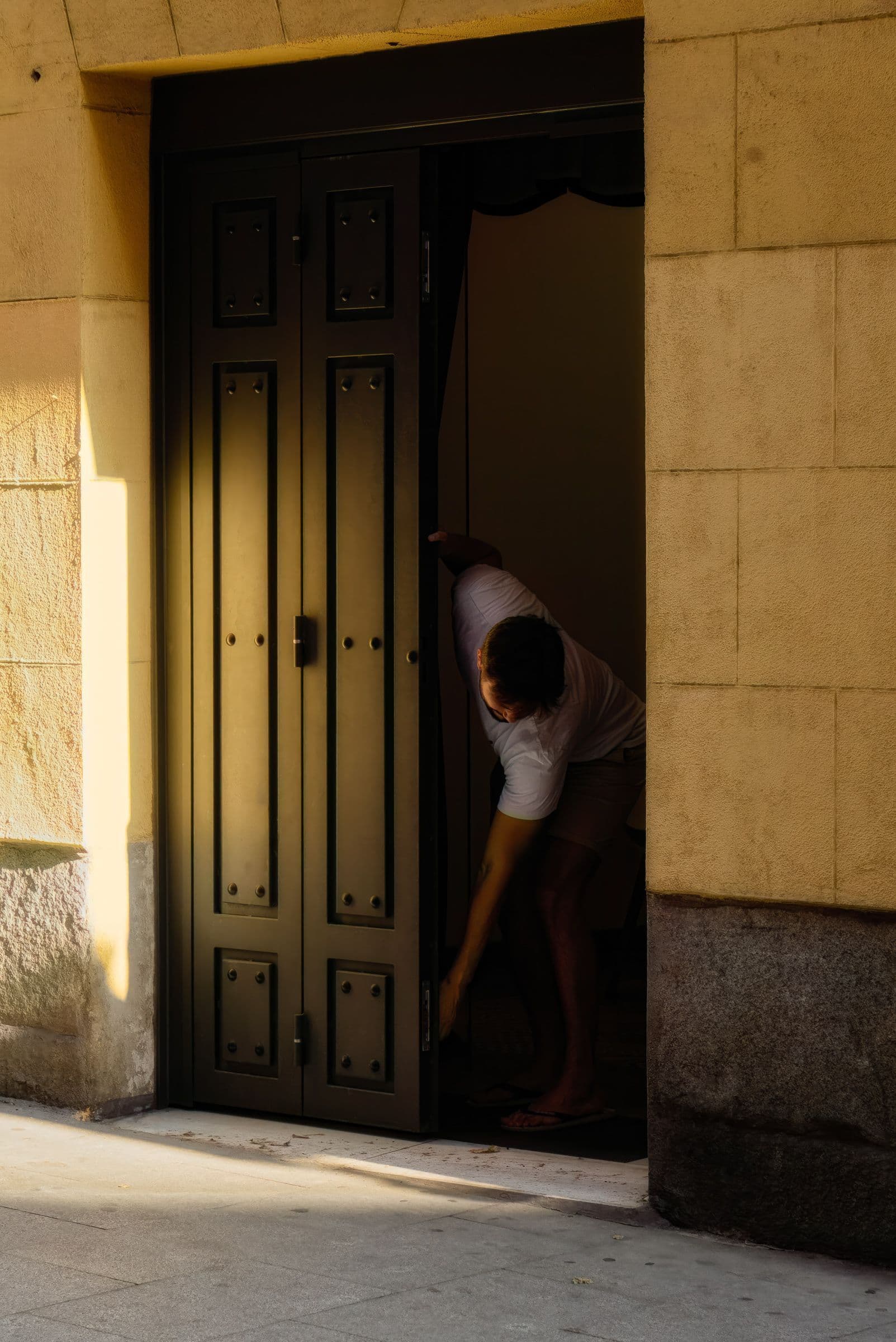 Man opening a sunlit dark door framed by warm stucco walls, creating contrast between shadow and light.