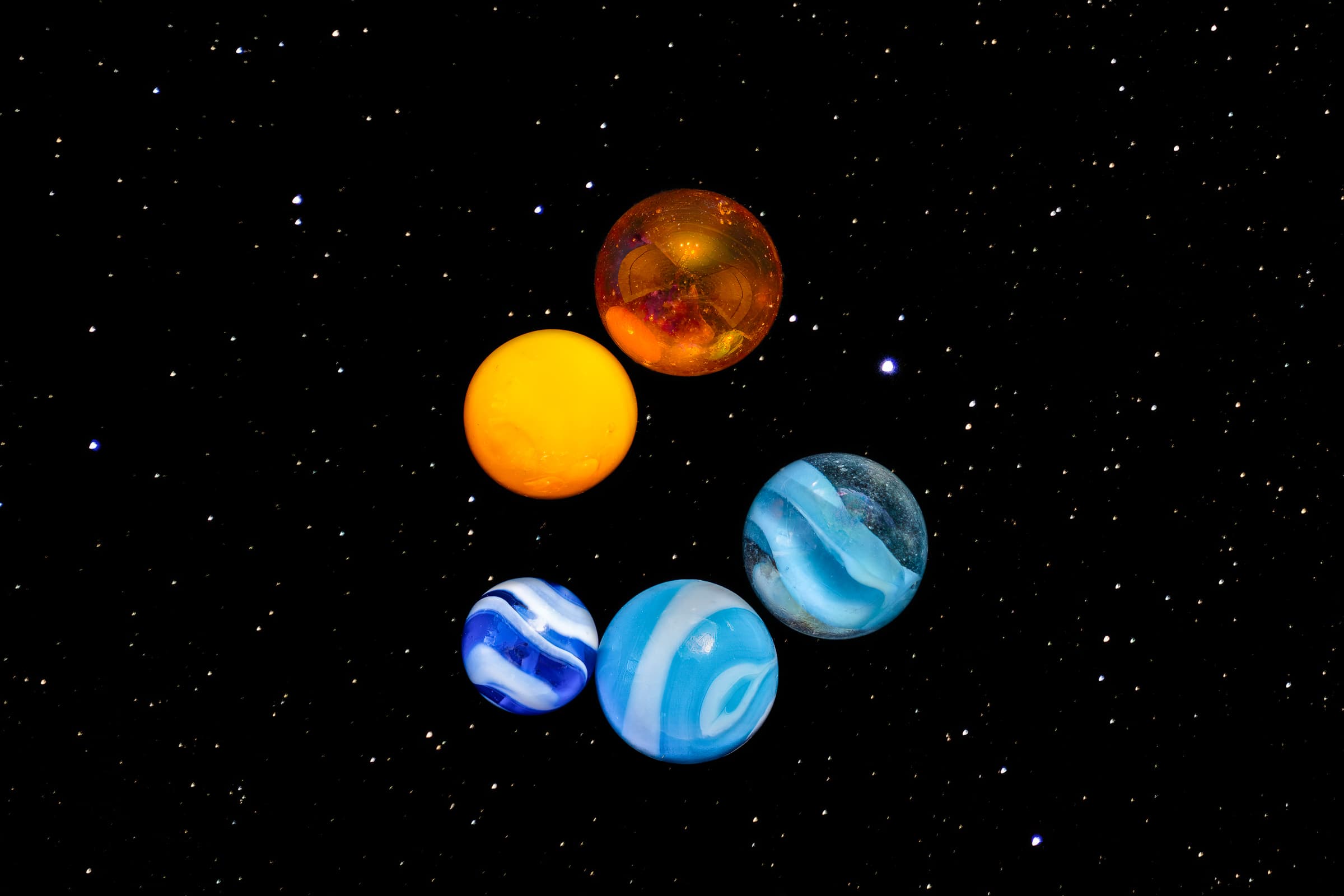 Five brightly-colored marbles appear to be hanging in space against a star-filled nightsky.