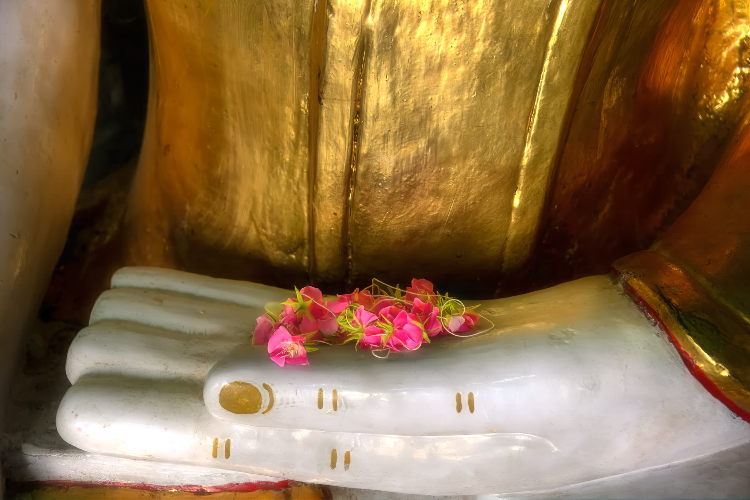 Umin Thone Ze Pagoda, Mandalay, Myanmar. Large hand of Buddha statue holds an offering of fresh pink flowers left as an offering by a visitor to the temple.