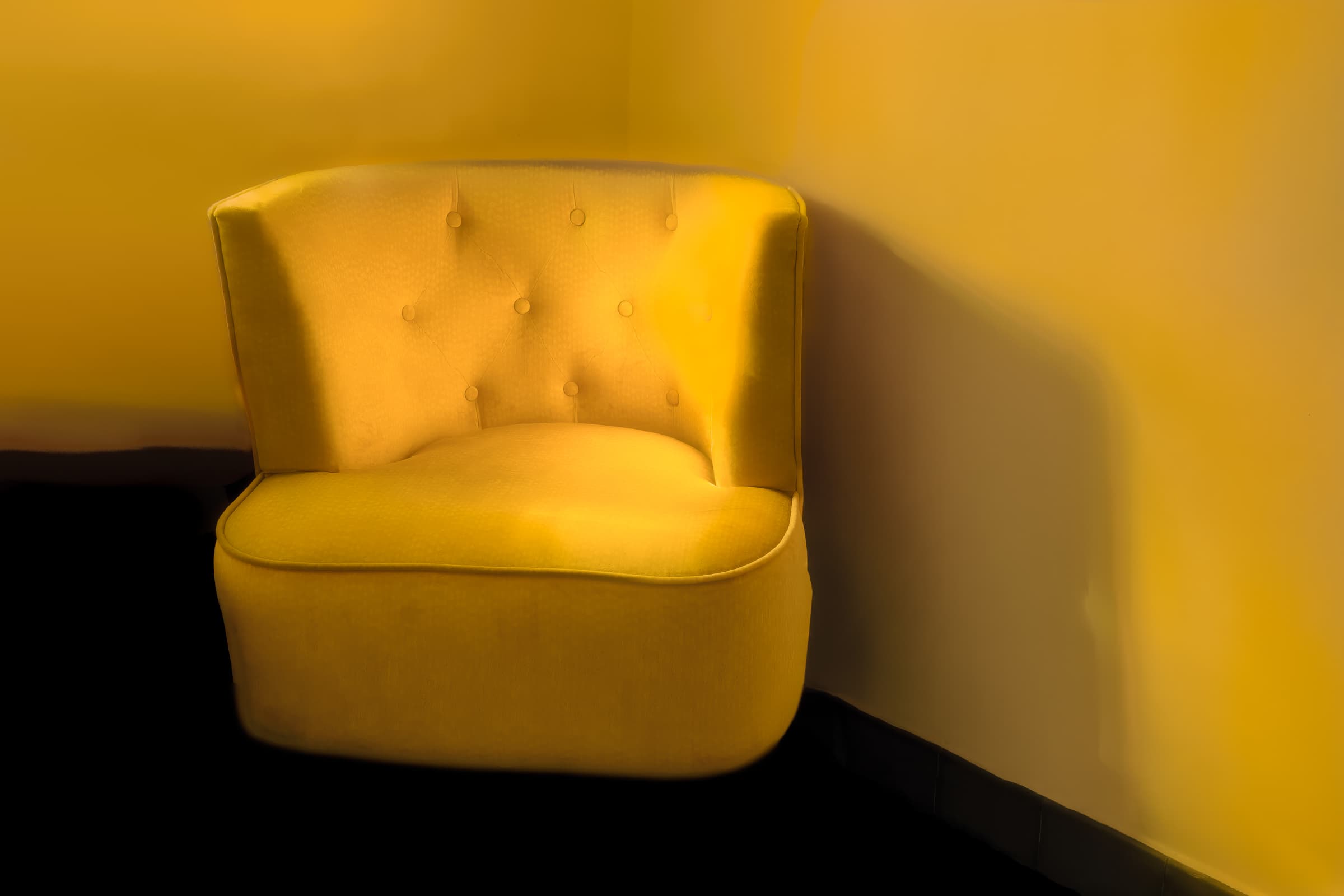 A yellow chair is illuminated by golden sunlight as it rests in the corner of a room. Soft light and gentle shadows spill across the chair and wall.