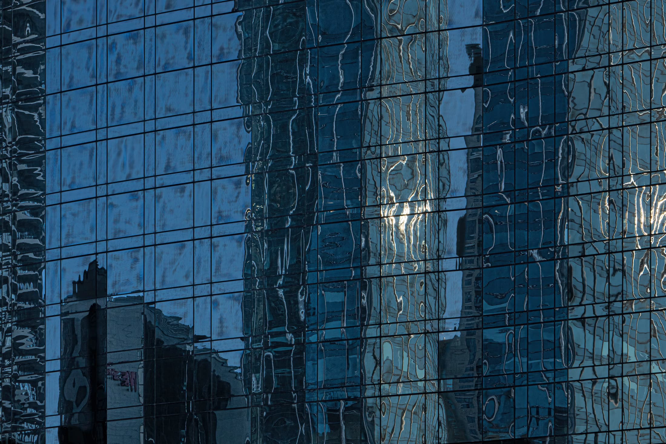 Chicago, Illinois. Reflections from nearby buildings (abstract, geometric, some distorted) on deep blue glass curtain wall as seen from the Chicago River.
